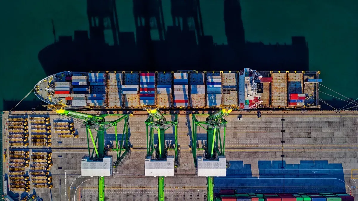 Aerial view of a cargo ship docked at a bustling port with stacked shipping containers
